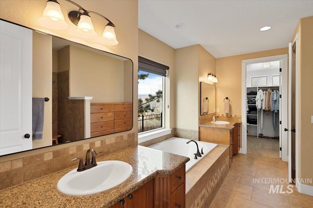 full bathroom featuring a bath, tile patterned flooring, a walk in closet, and a sink