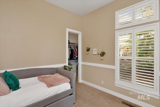 bedroom featuring a walk in closet, light colored carpet, visible vents, a textured ceiling, and baseboards