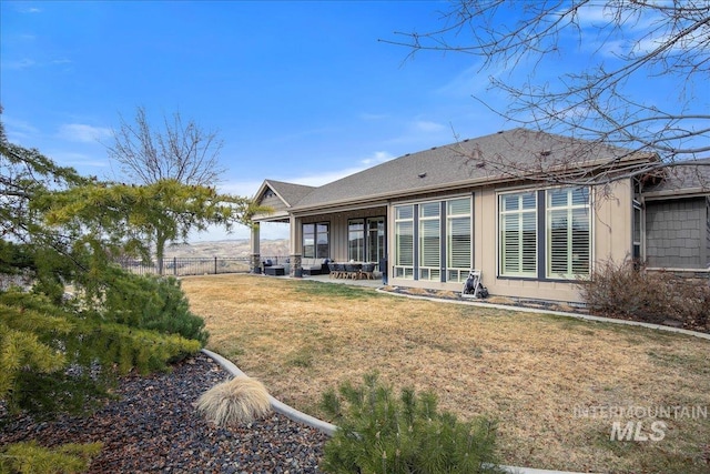 rear view of property featuring a shingled roof, a lawn, a patio area, and fence