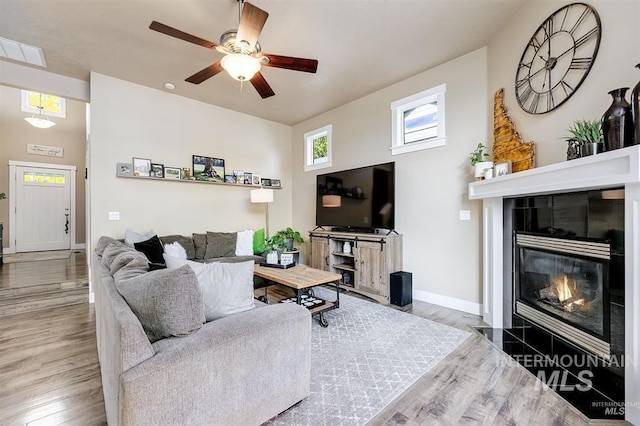 living area featuring visible vents, baseboards, a tiled fireplace, wood finished floors, and a ceiling fan