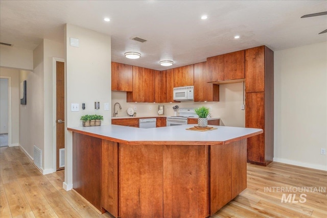 1134 N Camelot Dr, Boise, ID 83704 - kitchen with white appliances, light countertops, brown cabinets, light wood-style flooring, and a peninsula
