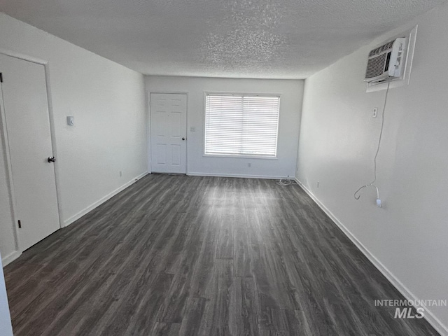 interior space with an AC wall unit, baseboards, a textured ceiling, and dark wood-style flooring