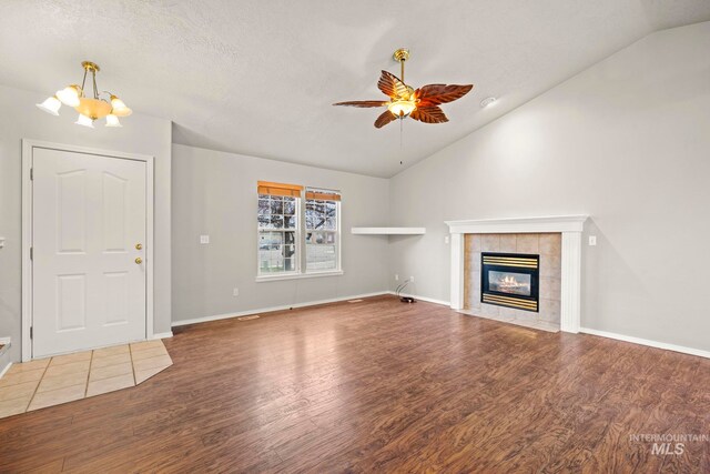 unfurnished living room with dark hardwood / wood-style floors, vaulted ceiling, a textured ceiling, a tiled fireplace, and ceiling fan with notable chandelier