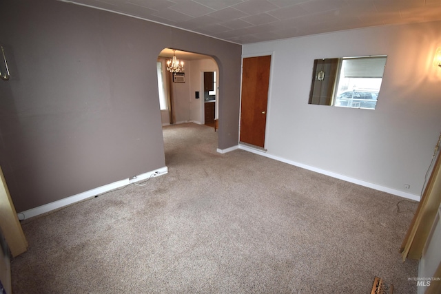 empty room featuring carpet flooring, baseboards, arched walkways, and a chandelier