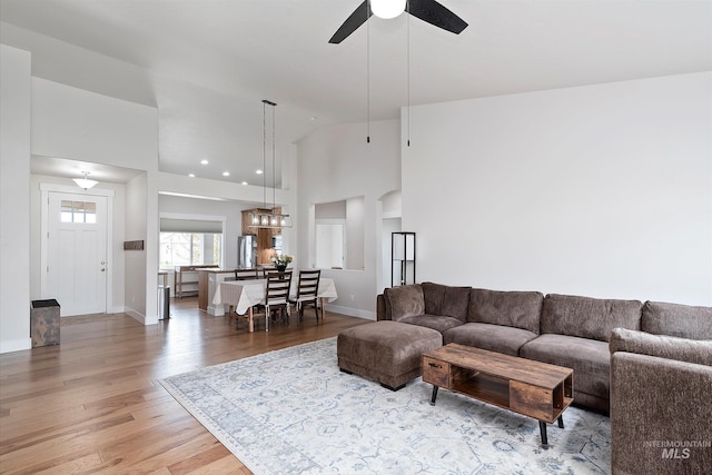 living room featuring high vaulted ceiling, ceiling fan, baseboards, and light wood-style flooring