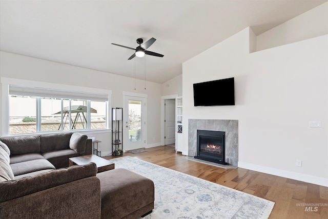 living area featuring lofted ceiling, wood finished floors, baseboards, a fireplace, and ceiling fan