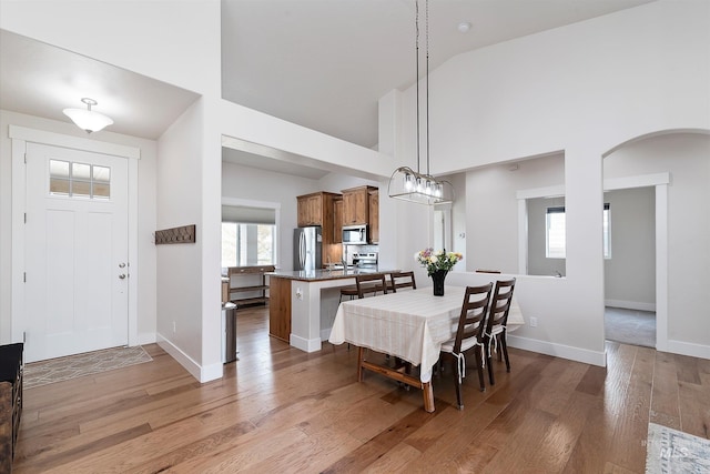 dining room featuring light wood-style flooring, baseboards, arched walkways, and high vaulted ceiling
