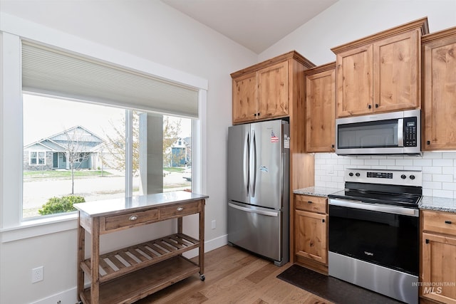kitchen with light stone countertops, light wood-style flooring, appliances with stainless steel finishes, and tasteful backsplash