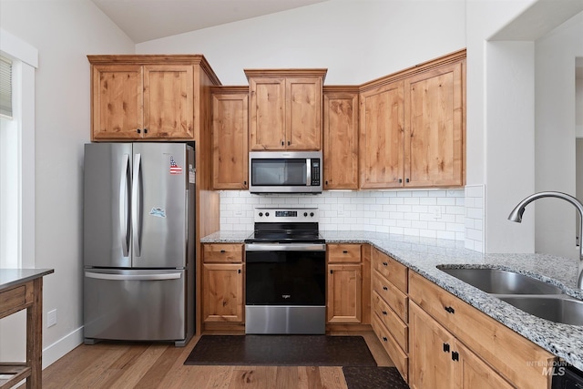 kitchen with light stone counters, a sink, decorative backsplash, stainless steel appliances, and lofted ceiling