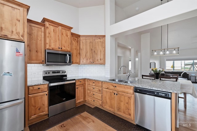 kitchen featuring a sink, decorative backsplash, a peninsula, appliances with stainless steel finishes, and open floor plan