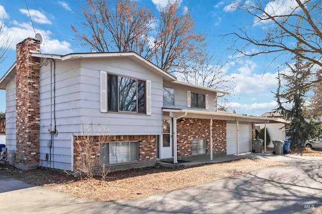 split level home featuring driveway, brick siding, a chimney, and an attached garage