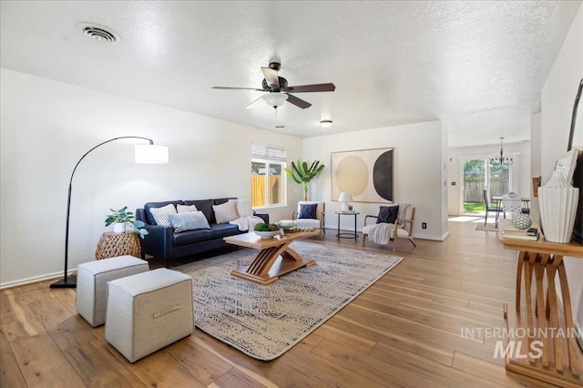 living room with visible vents, ceiling fan with notable chandelier, a textured ceiling, and wood finished floors