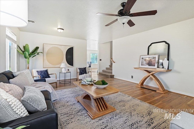 living area featuring visible vents, ceiling fan, baseboards, stairs, and wood finished floors