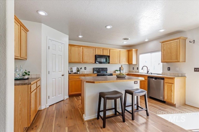 kitchen with a kitchen island, a kitchen breakfast bar, light wood-style floors, black appliances, and a sink