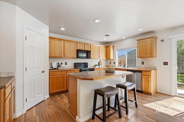 kitchen with a kitchen bar, black appliances, light wood-style flooring, and plenty of natural light