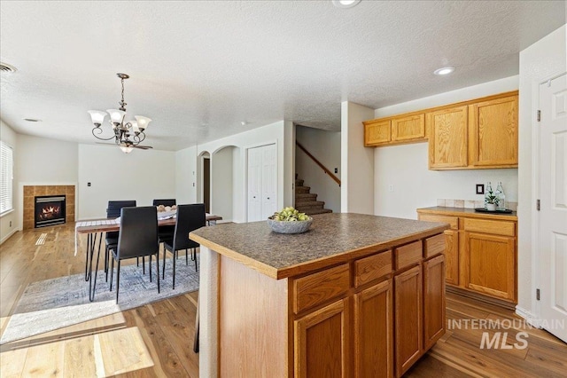 kitchen with a textured ceiling, dark countertops, arched walkways, a fireplace, and light wood finished floors