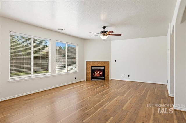 unfurnished living room with a tiled fireplace, visible vents, a textured ceiling, and wood finished floors