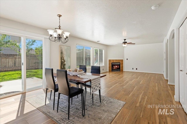 dining area with light wood finished floors, baseboards, ceiling fan with notable chandelier, a fireplace, and a textured ceiling