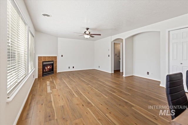 unfurnished living room featuring visible vents, arched walkways, a fireplace, and hardwood / wood-style flooring