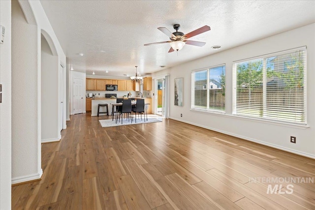 unfurnished living room featuring light wood-type flooring, baseboards, a textured ceiling, and ceiling fan with notable chandelier