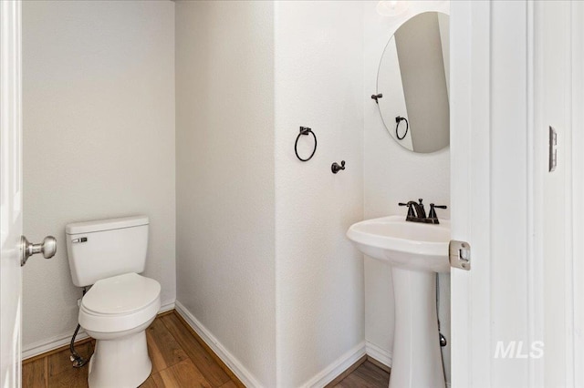 half bath with toilet, wood finished floors, and baseboards