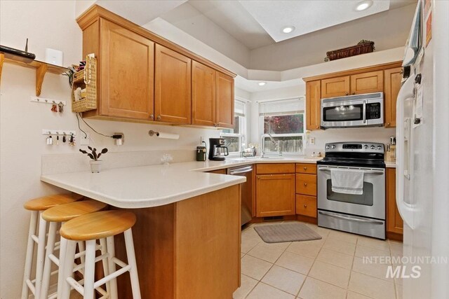 3012 Myrtlewood Way, Nampa, ID 83686 - kitchen featuring appliances with stainless steel finishes, a peninsula, light tile patterned flooring, a kitchen bar, and a sink