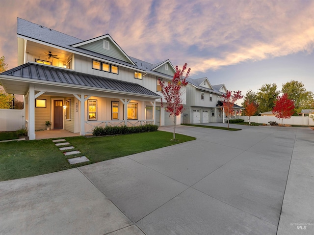 rear view of property with board and batten siding, a standing seam roof, covered porch, a lawn, and fence