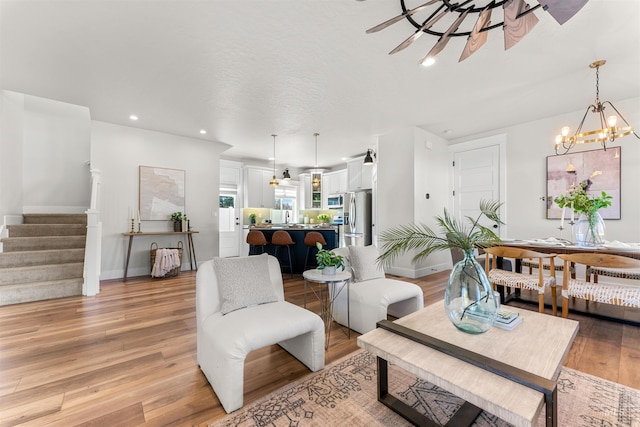 living area with baseboards, recessed lighting, stairway, light wood-style flooring, and ceiling fan with notable chandelier