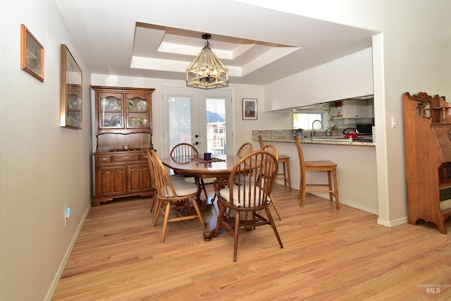 dining area featuring sink, light hardwood / wood-style floors, french doors, a raised ceiling, and a chandelier