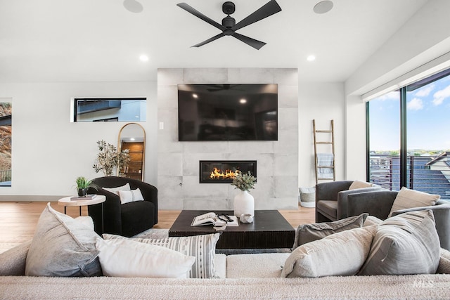 living room featuring a tiled fireplace, light hardwood / wood-style flooring, and ceiling fan