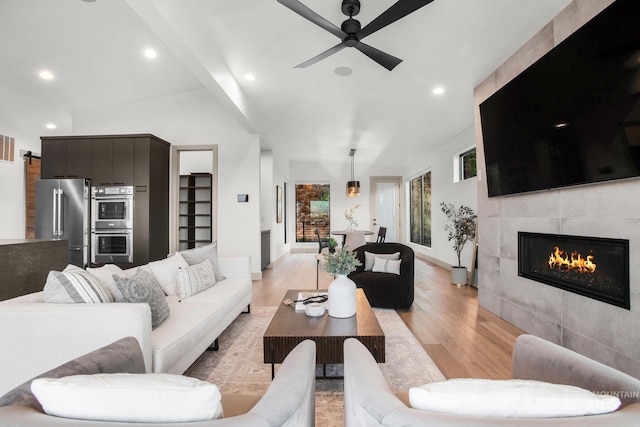 living room with a tiled fireplace, light hardwood / wood-style flooring, lofted ceiling, and ceiling fan