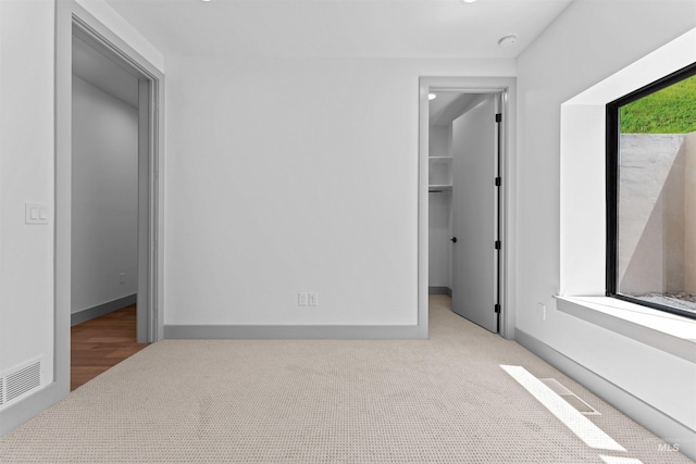 unfurnished bedroom featuring a spacious closet, light carpet, and a closet