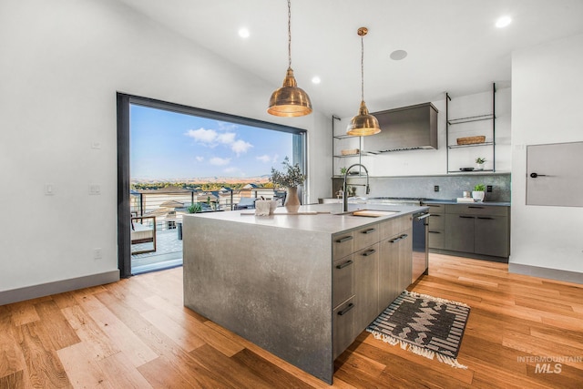 kitchen with gray cabinetry, light hardwood / wood-style flooring, pendant lighting, a kitchen island with sink, and backsplash