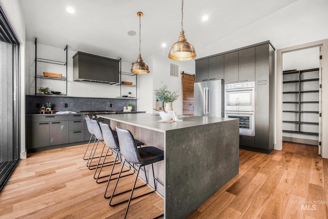 kitchen with a kitchen island, pendant lighting, a kitchen breakfast bar, premium appliances, and light hardwood / wood-style flooring