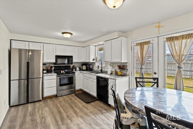 kitchen featuring a textured ceiling, sink, black appliances, hardwood / wood-style floors, and white cabinetry