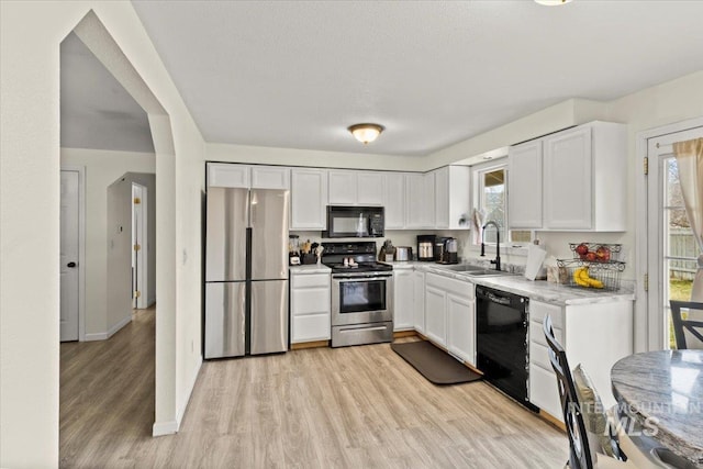 kitchen with black appliances, white cabinets, sink, light stone countertops, and light wood-type flooring