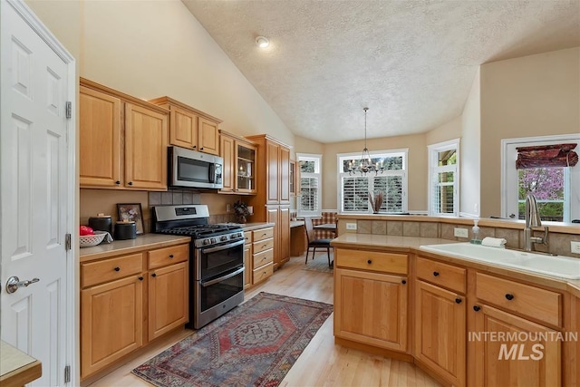 kitchen with appliances with stainless steel finishes, vaulted ceiling, a sink, light wood finished floors, and a notable chandelier
