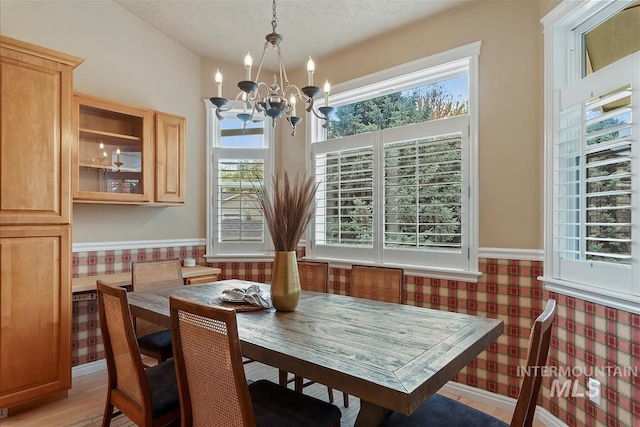 dining area with a textured ceiling, a wainscoted wall, a notable chandelier, and a healthy amount of sunlight