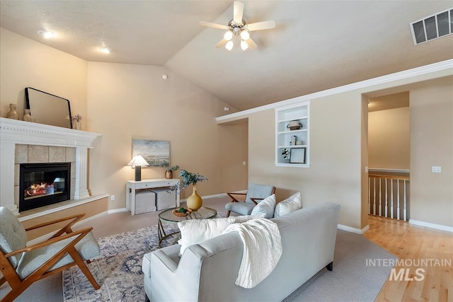 living area with ceiling fan, baseboards, lofted ceiling, a tile fireplace, and visible vents