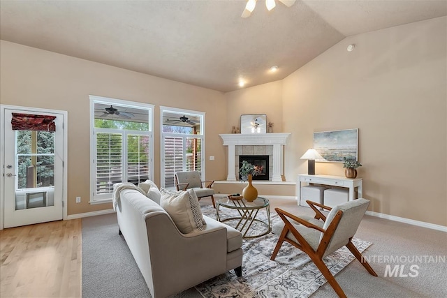 living area featuring a tiled fireplace, baseboards, ceiling fan, and vaulted ceiling