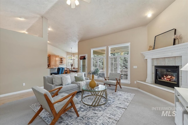 living room with baseboards, a textured ceiling, a tiled fireplace, ceiling fan with notable chandelier, and vaulted ceiling