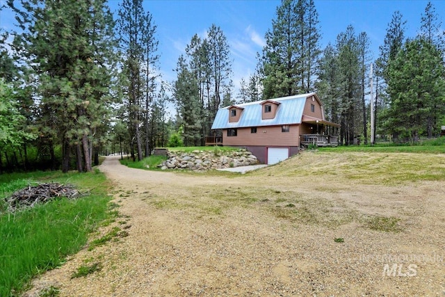 76 W Castle Creek Rd, Garden Valley, ID 83622 - view of side of home featuring dirt driveway, a gambrel roof, an attached garage, metal roof, and view of wooded area