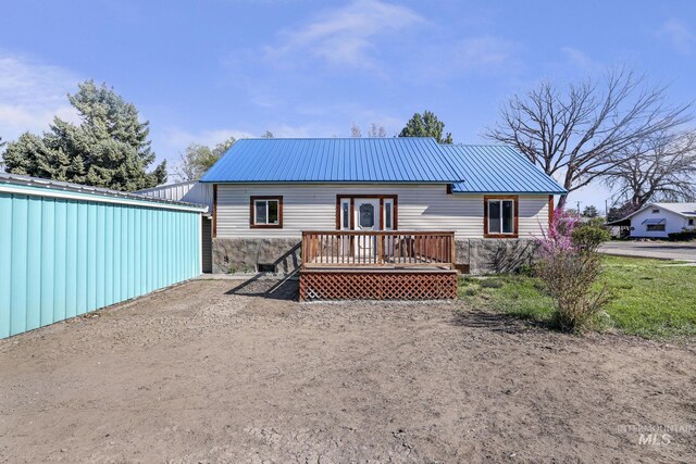 back of house featuring stone siding, a deck, and metal roof