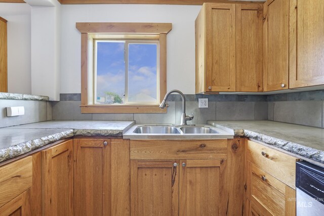 kitchen featuring brown cabinets, stainless steel dishwasher, a sink, and backsplash
