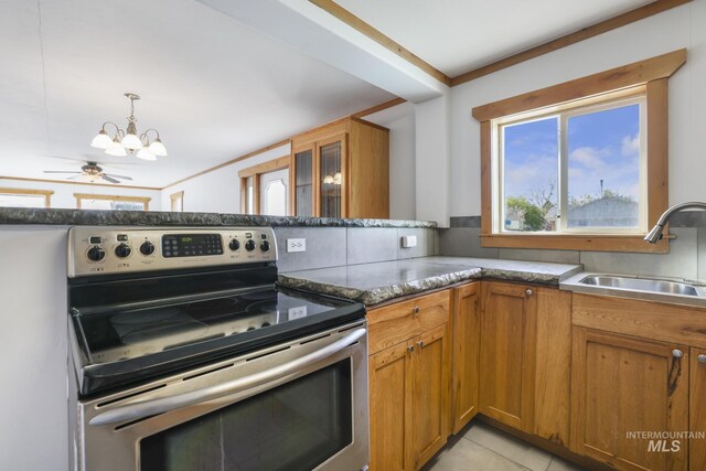 kitchen with a sink, dark stone countertops, an inviting chandelier, stainless steel range with electric stovetop, and brown cabinetry