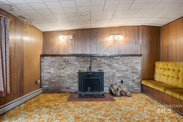 unfurnished living room with a baseboard heating unit, carpet, a wood stove, and wooden walls