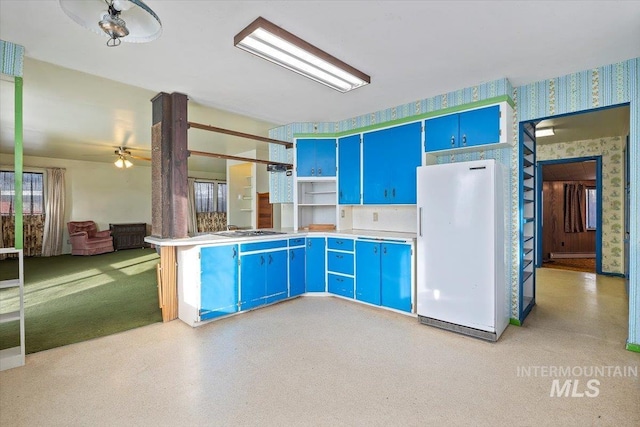 kitchen with blue cabinetry, open shelves, freestanding refrigerator, a peninsula, and wallpapered walls