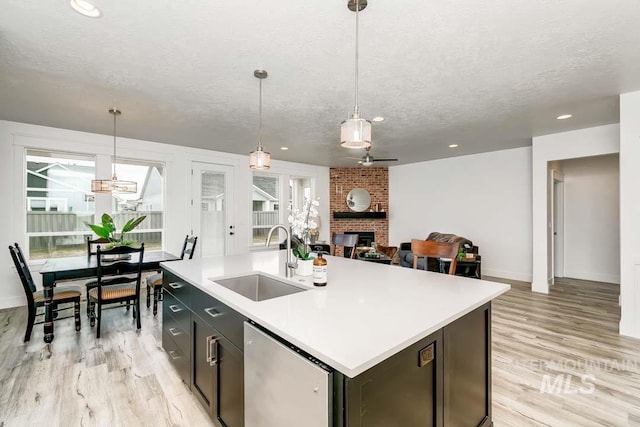 kitchen featuring sink, a brick fireplace, hanging light fixtures, a textured ceiling, and a kitchen island with sink