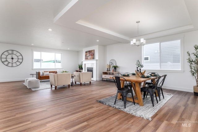 dining area featuring a fireplace, a tray ceiling, wood finished floors, and baseboards