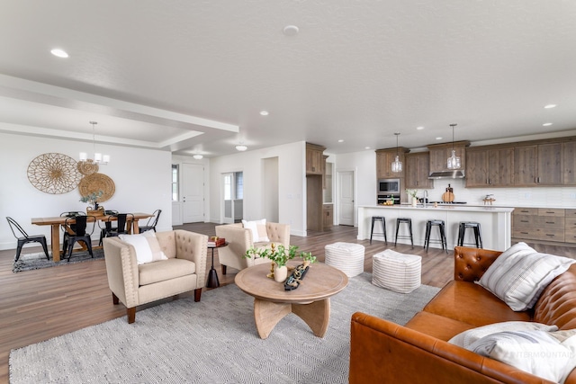 living area featuring a tray ceiling, wood finished floors, recessed lighting, baseboards, and a chandelier